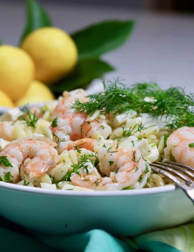 Shrimp pasta salad in a bowl with another bowl of lemons in the background.