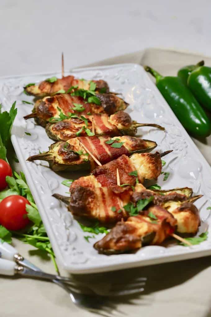 Baked Jalapeno Poppers wrapped in bacon on a white serving plate.