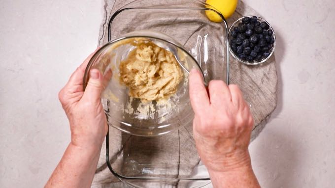 Pouring a butter and flour mixture into a clear glass baking dish. 