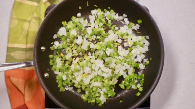The holy trinity, onion, bell pepper, and celery cooking in a skillet. 