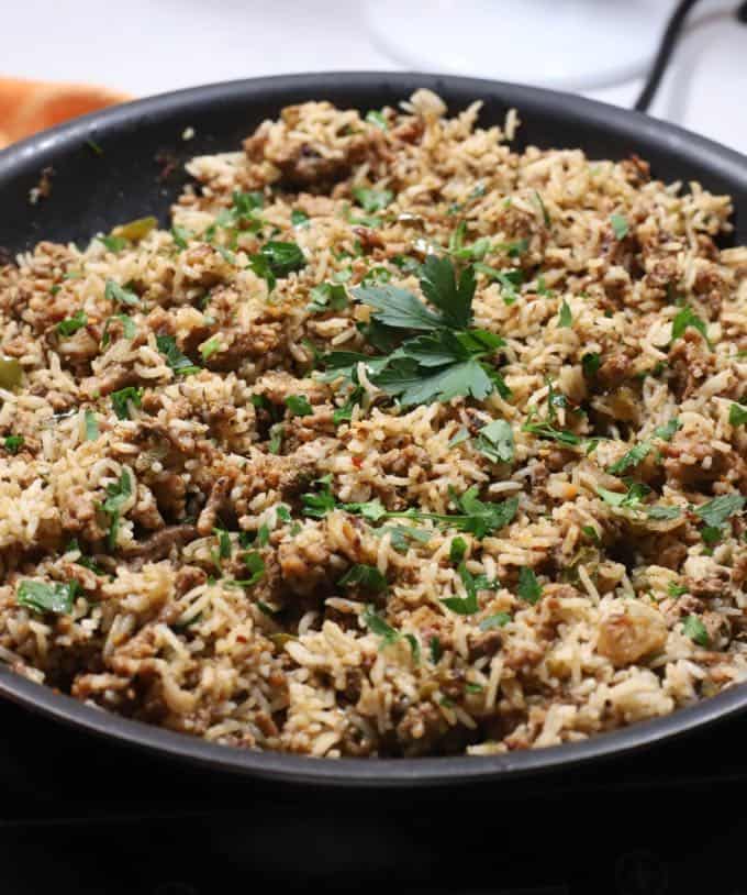 A large skillet full of dirty rice topped with parsley. 