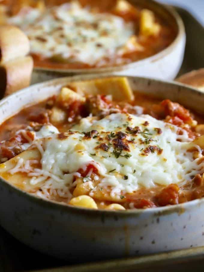 Lasagna soup in two bowls topped with melted mozzarella cheese.
