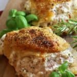Stuffed chicken breasts on a wooden cutting board garnished with basil and rosemary.