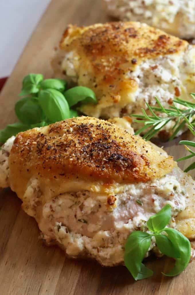 Stuffed chicken breasts on a wooden cutting board garnished with basil and rosemary.