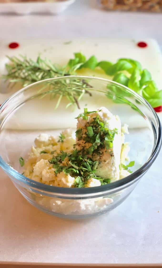 A clear glass bowl with Boursin cheese and fresh herbs.