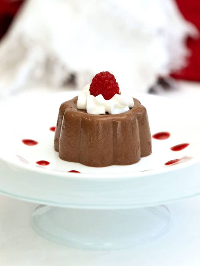 Chocolate Blancmange on a white plate topped with whipped cream and a raspberry.