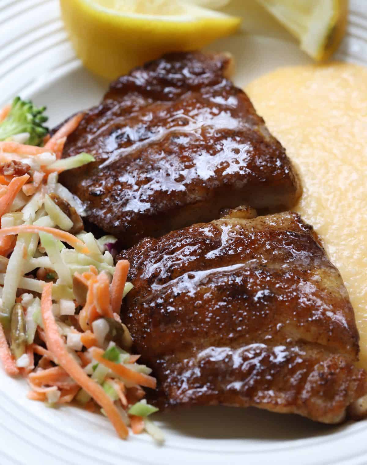 Blackened mahi-mahi fillets on a white plate with cheese grits and broccoli slaw. 