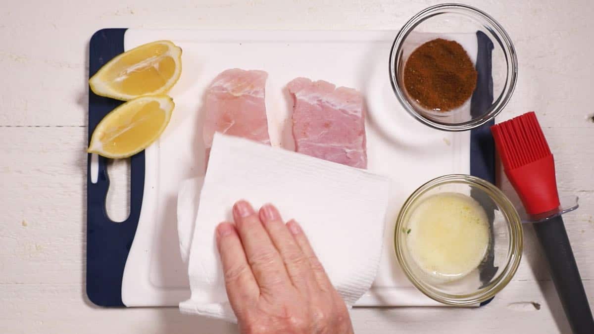 Using a paper towel to pat dry two fish fillets.