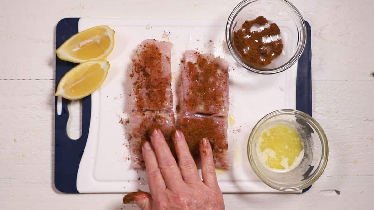 Adding blackened seasoning to two fish fillets on a cutting board.