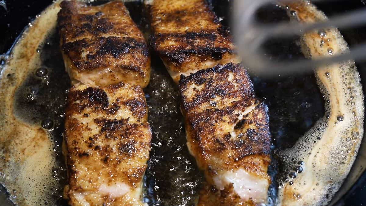 Two blackened fish fillets in a cast iron skillet.