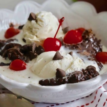 A white bowl with chocolate dump cake topped with vanilla ice cream and cherries.