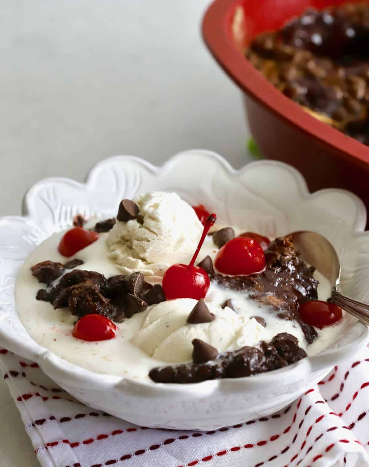 Chocolate Cherry Dump Cake topped with vanilla ice cream in a white bowl. 