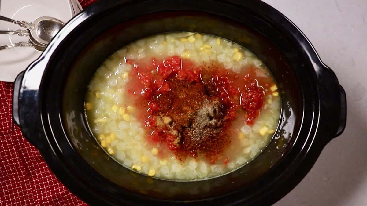 A crockpot wth chicken stock, corn, canned tomatoes and various seasonings.