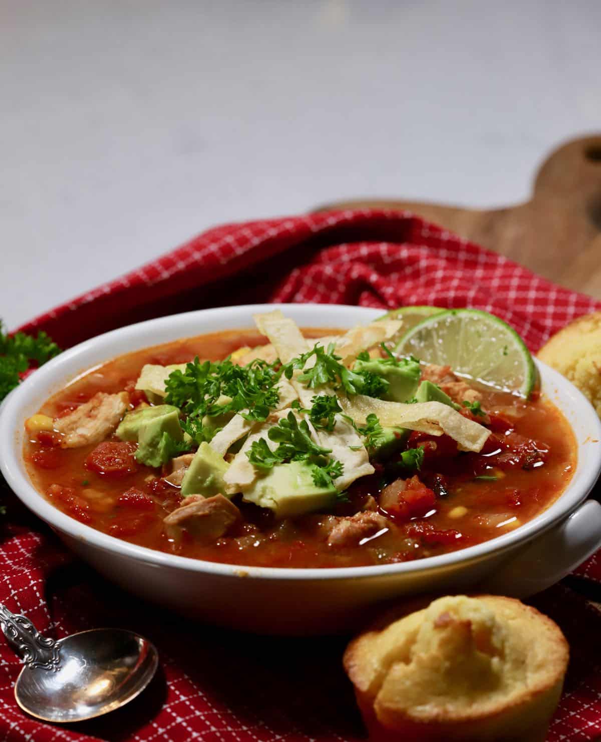 A white bowl with chicken tortilla soup topped with avocado and tortilla strips.