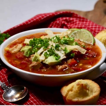 A bowl of chicken tortilla soup, topped with tortilla strips, avocado and cilantro.