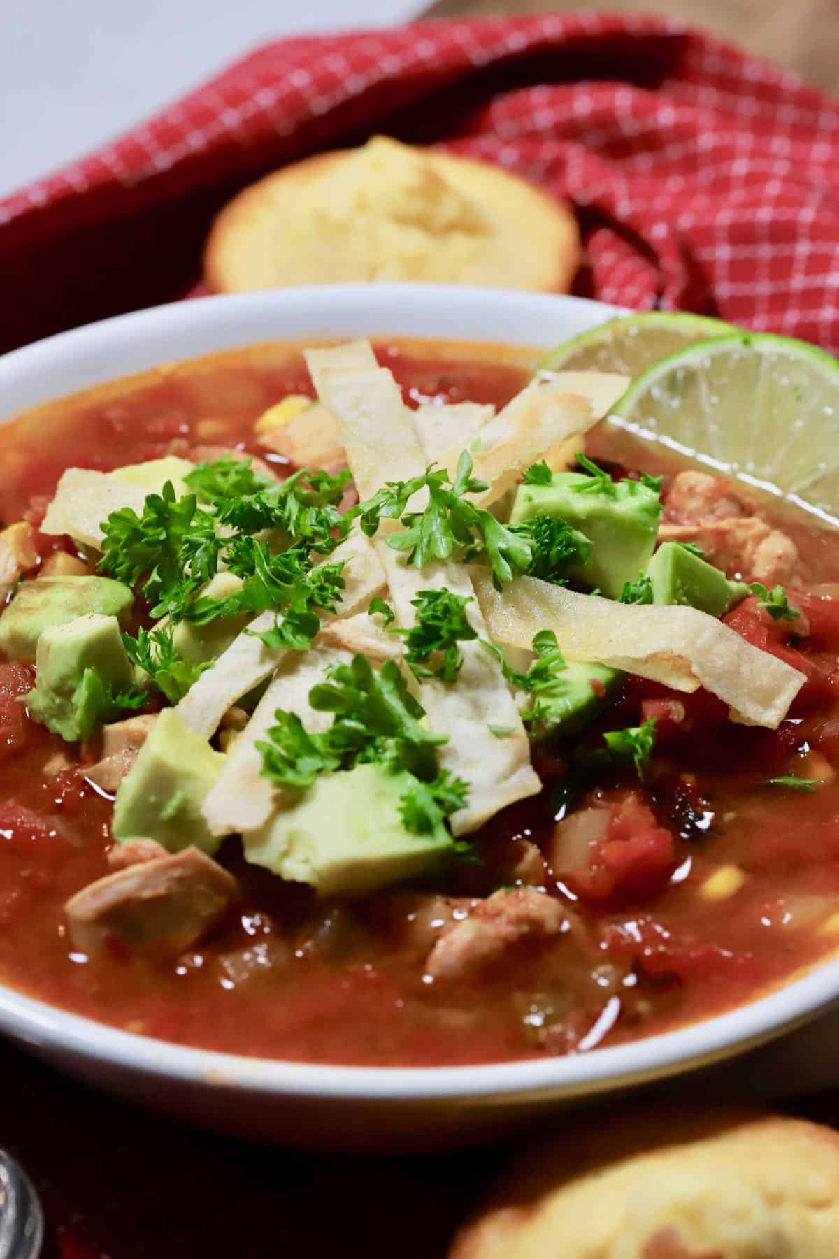 A bowl of chicken tortilla soup in a white bowl on a red napkin.