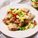 Two grouper fillets on a white plate topped with mango salsa.