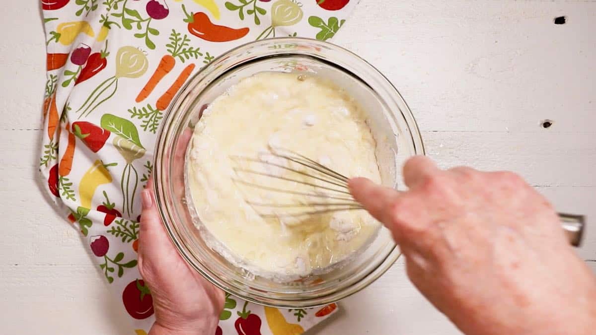 Mixing cornmeal pancake batter in a clear glass bowl.