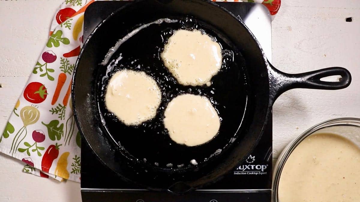 Cornmeal pancakes cooking in a cast-iron skillet.