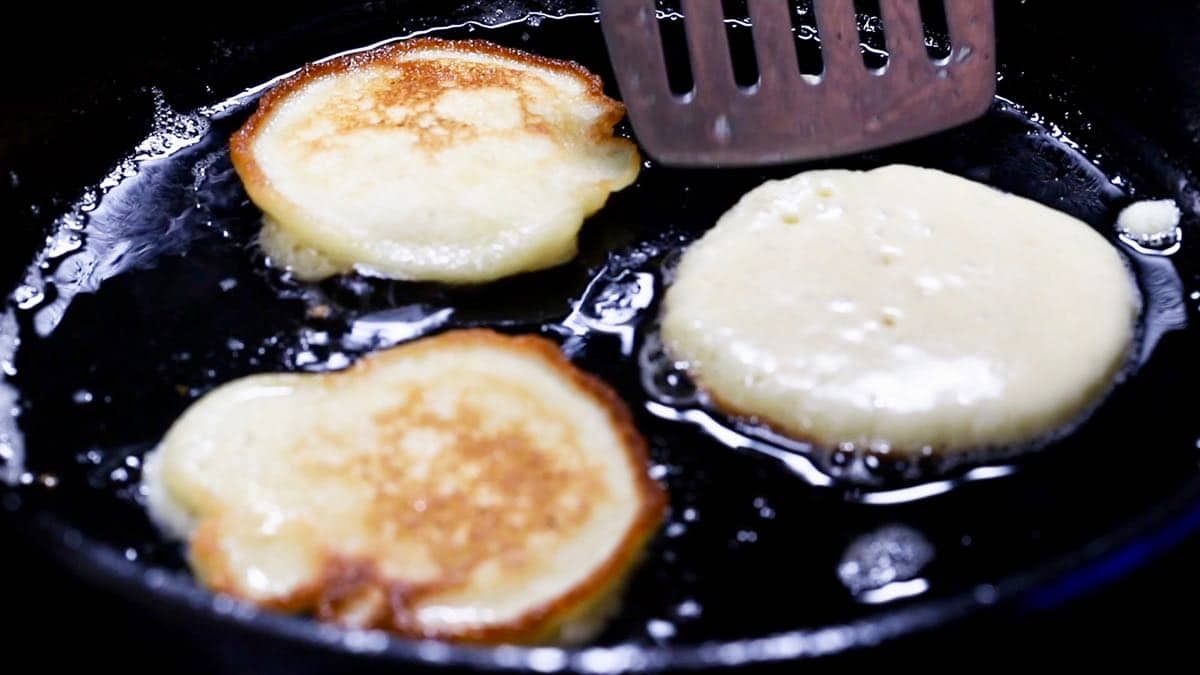 Cooking fried cornbread in a cast-iron skillet.