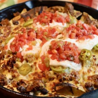 Nachos cooked in a cast-iron skillet and topped with sour cream and salsa.