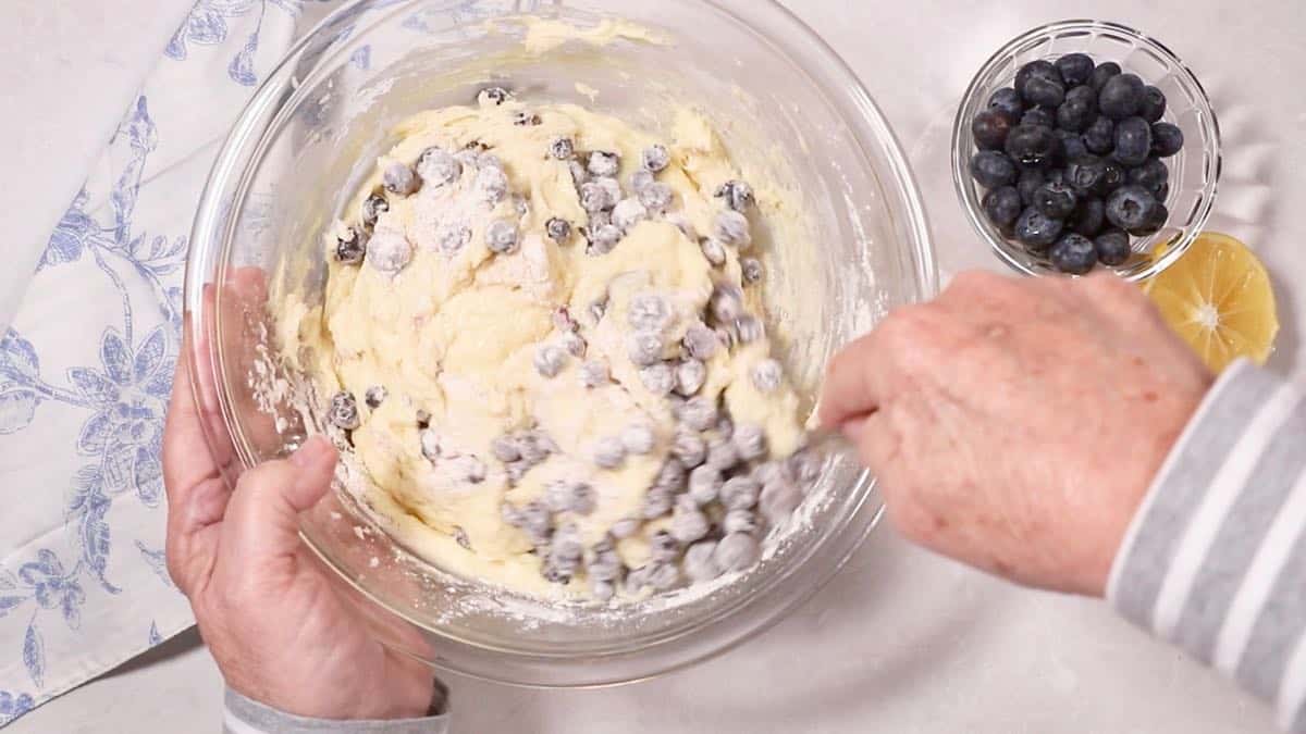 Stirring blueberries into bread batter in a clear glass mixing bowl. 