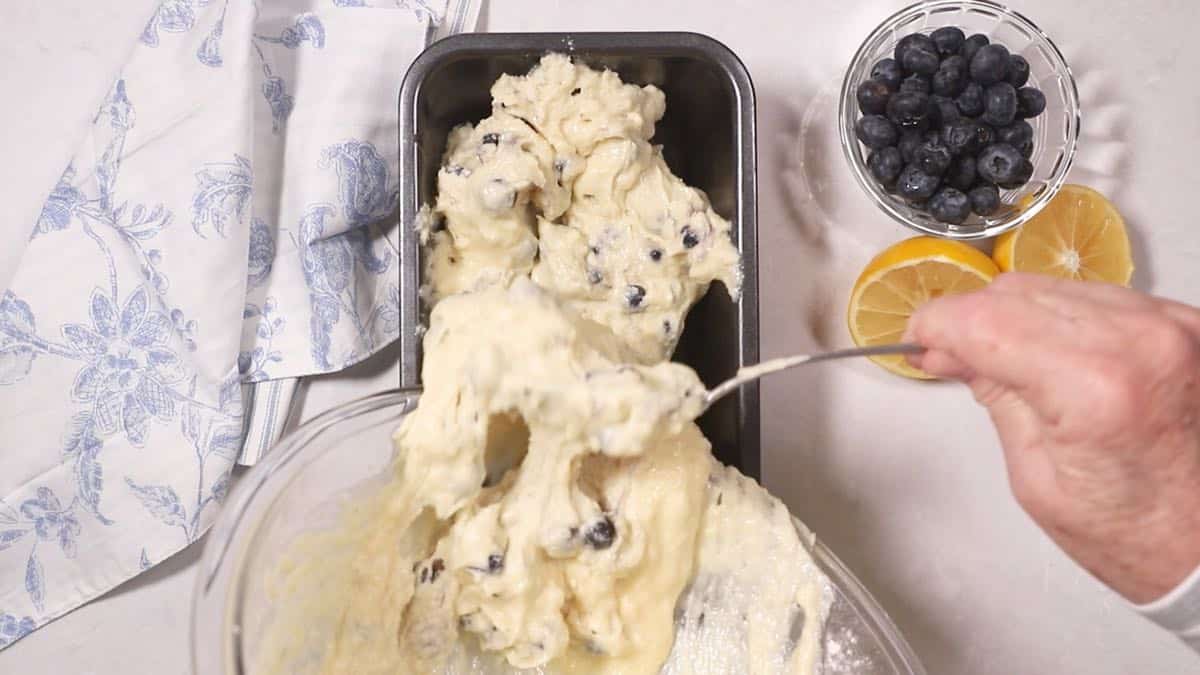 Adding batter with blueberries to a loaf pan. 