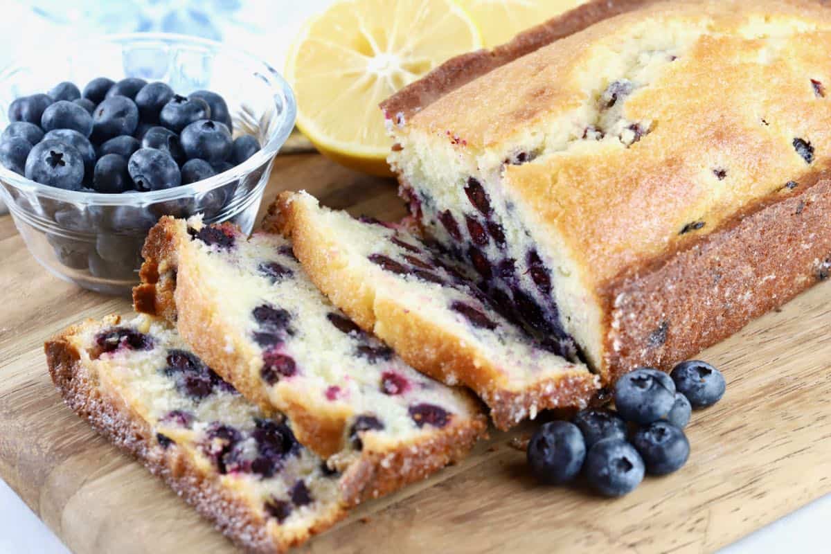 A loaf of blueberry bread sliced on a cutting board. 