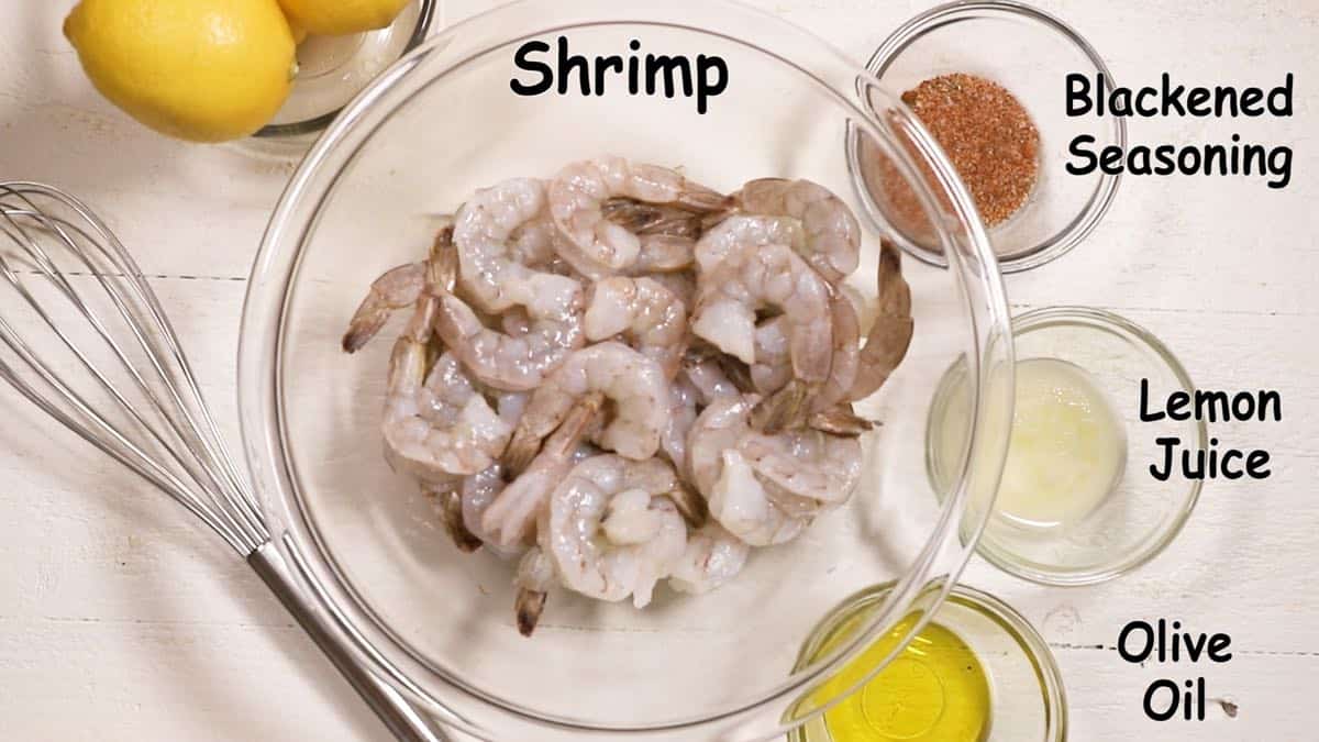 A large bowl of raw shrimp with seasoning, olive oil and lemon juice in smaller bowls. 