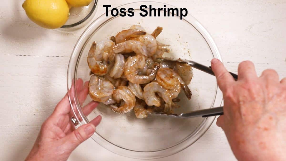 A glass bowl with raw shrimp in a marinade.