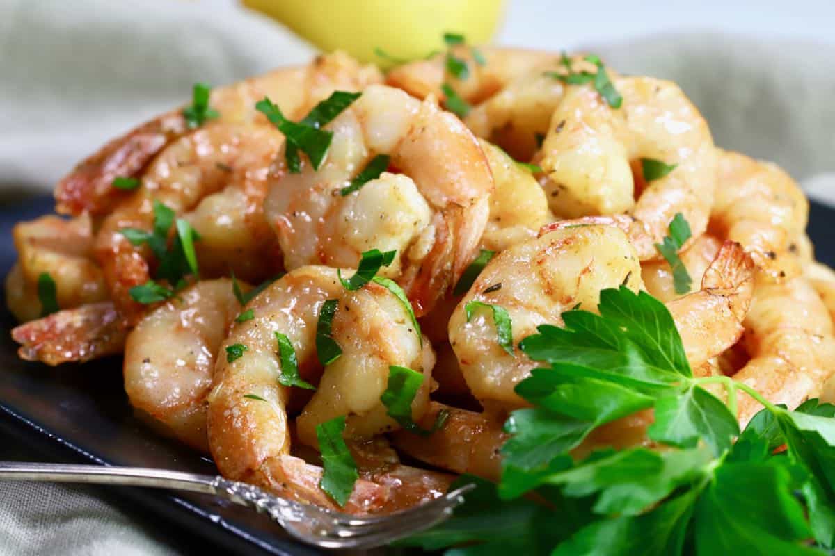 A black plate with smoked shrimp topped with parsley. 