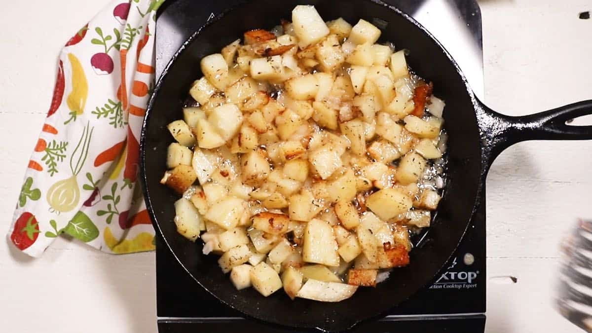 A cast-iron skillet with potatoes frying.