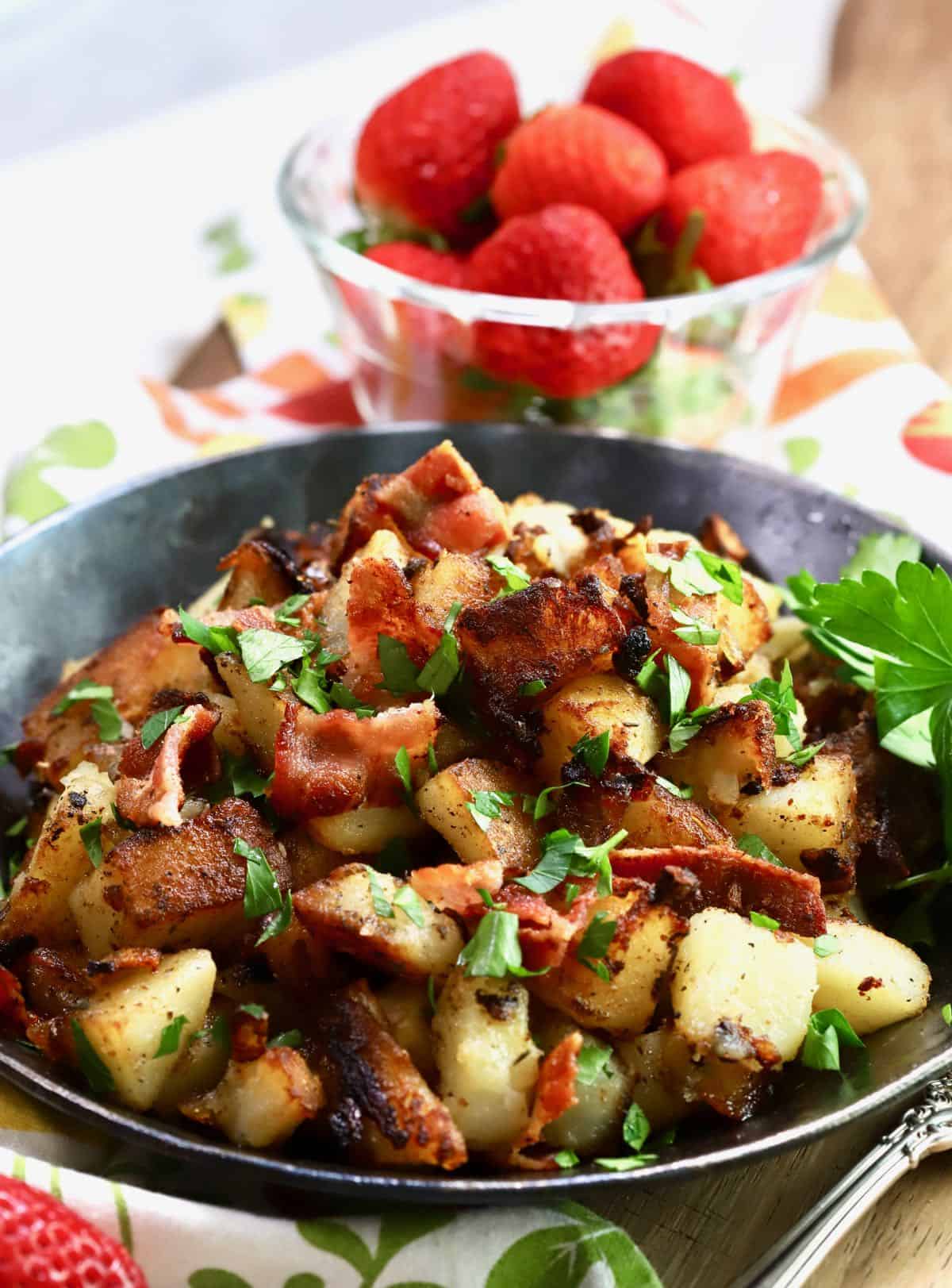 A cast-iron pan with fried potatoes topped with bacon and parsley. 