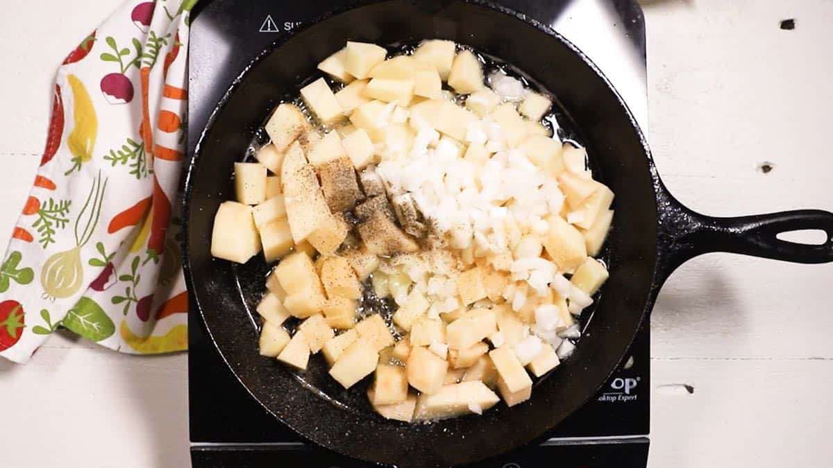 Cubed potatoes and onions in a cast-iron pan cooking on the stove.