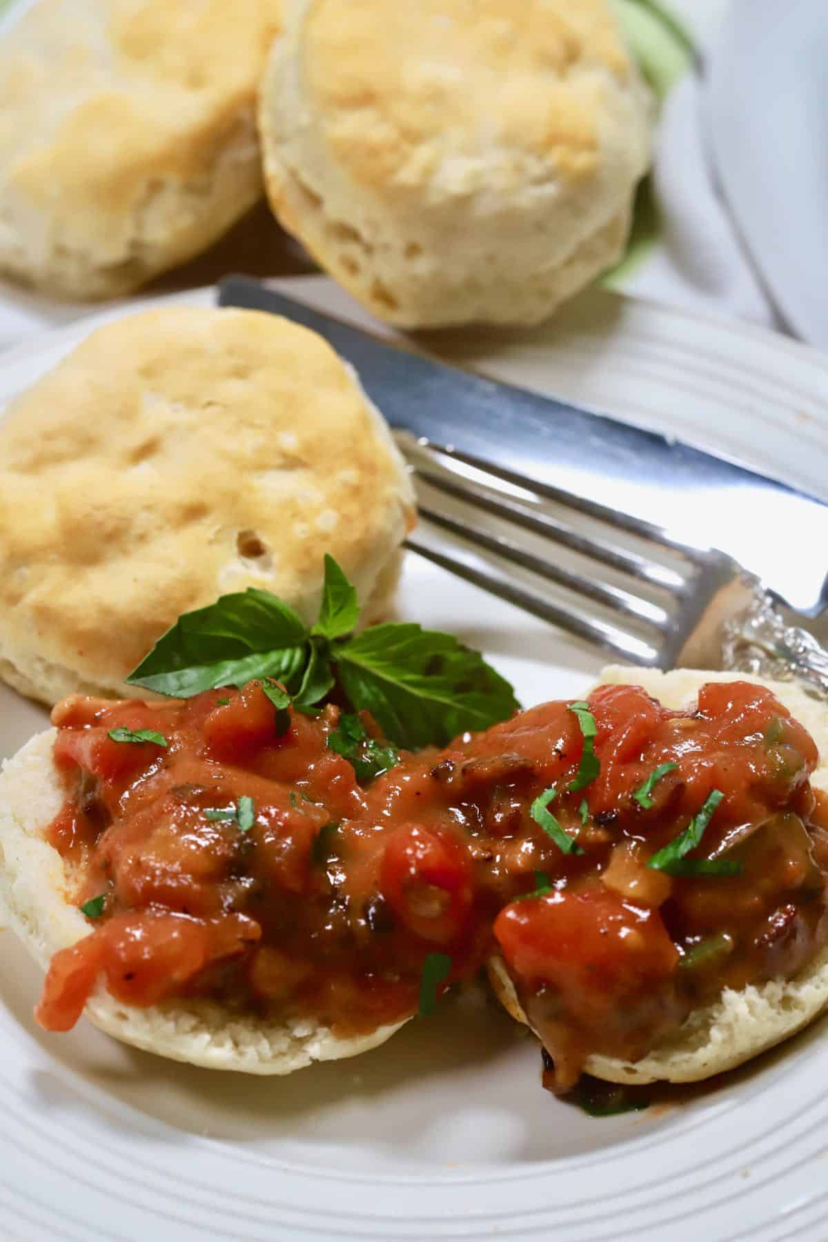 Several halved biscuits topped with tomato gravy and garnished with sprigs of basil. 