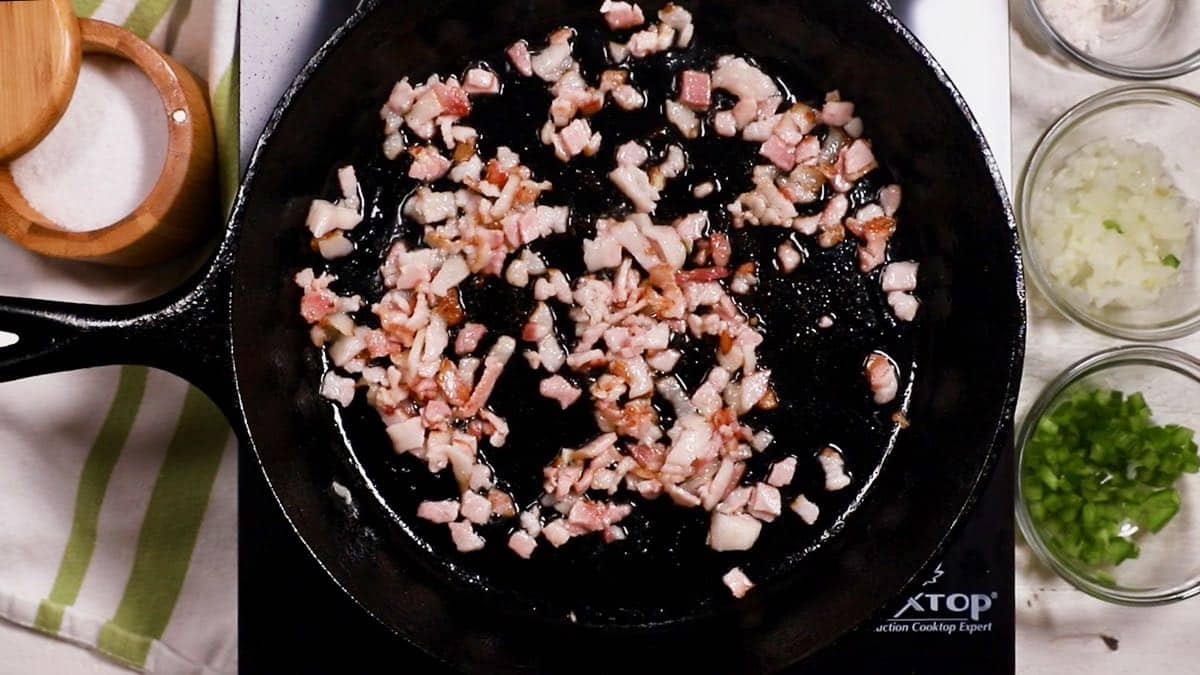 Chopped bacon cooking in a cast-iron skillet.