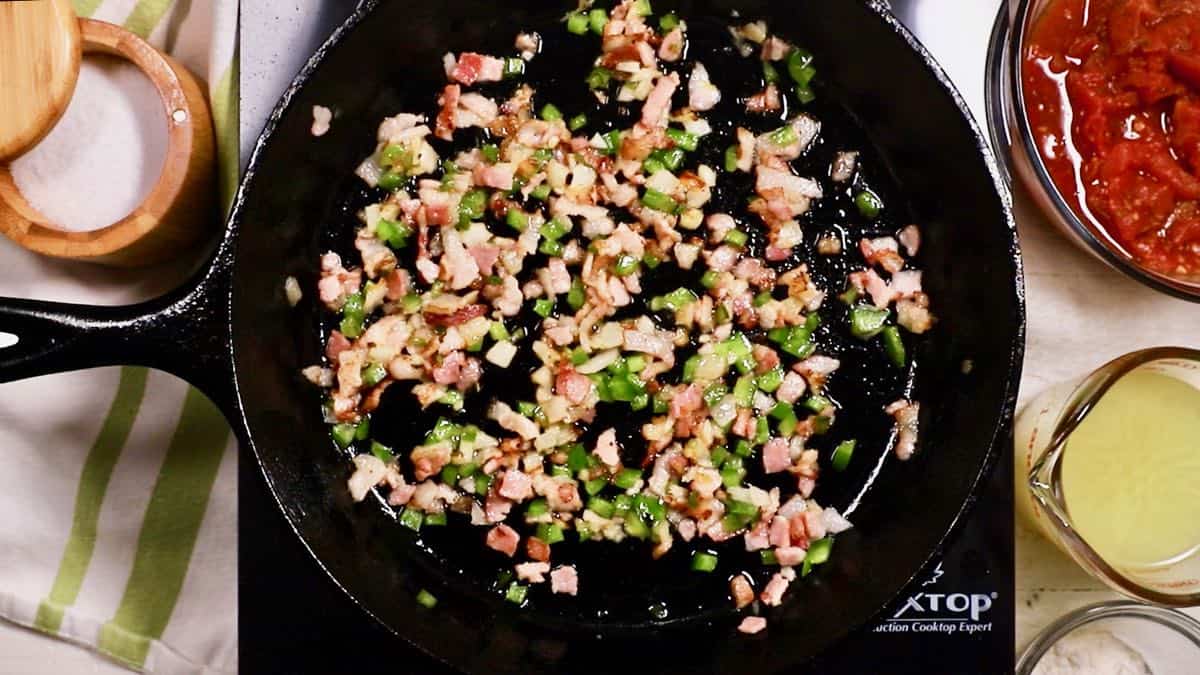 Bacon, bell pepper and onion cooking in a cast iron skillet.