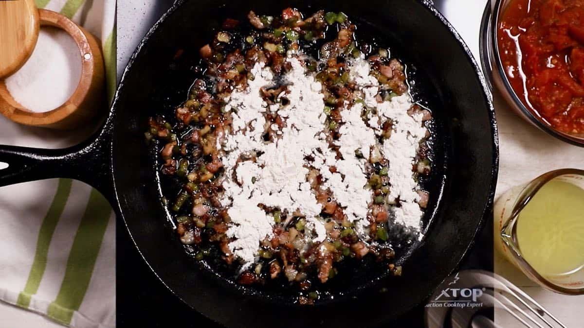 A cast iron skillet with peppers and onions and flour cooking.