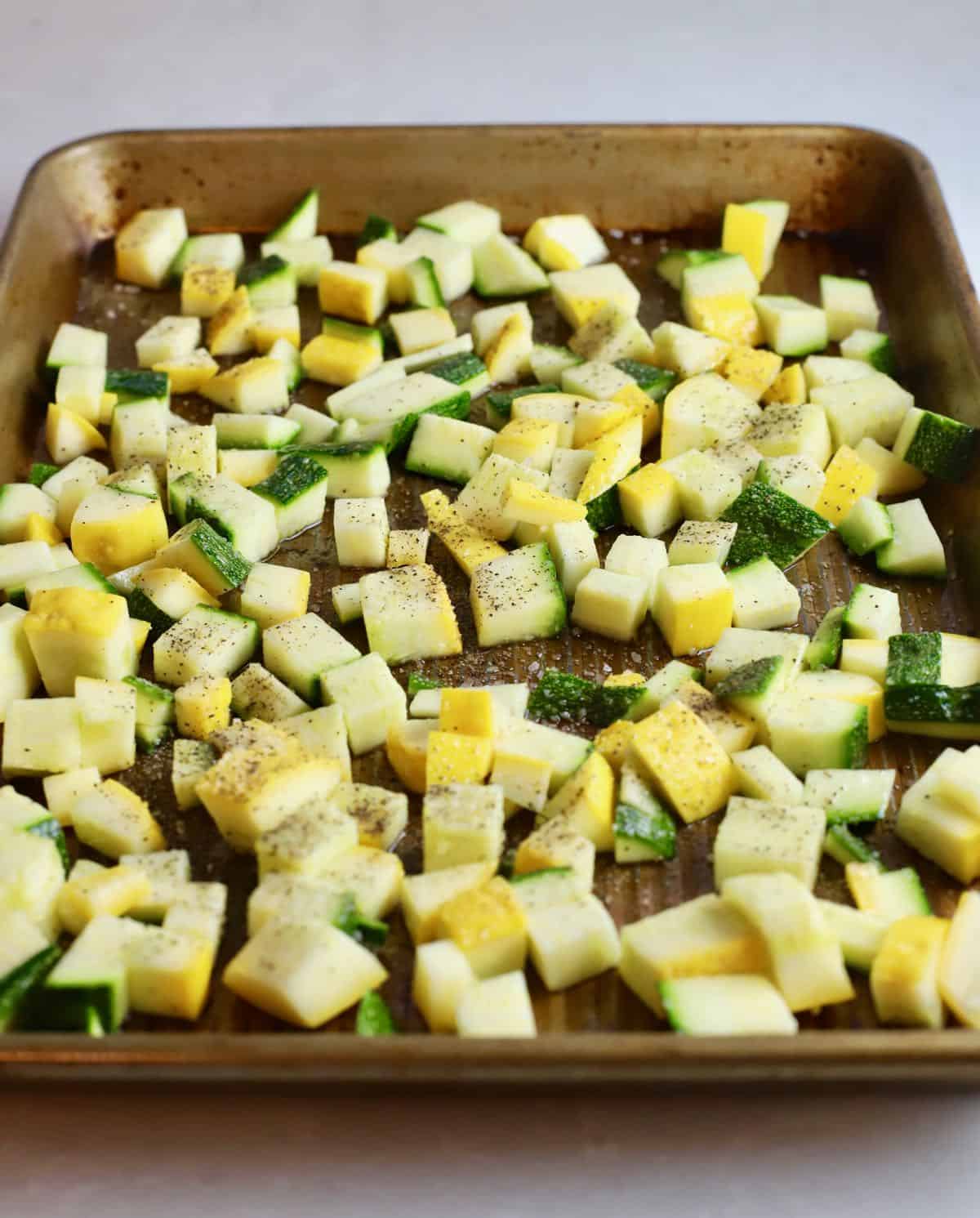 Chopped yellow and zucchini squash on a baking sheet. 