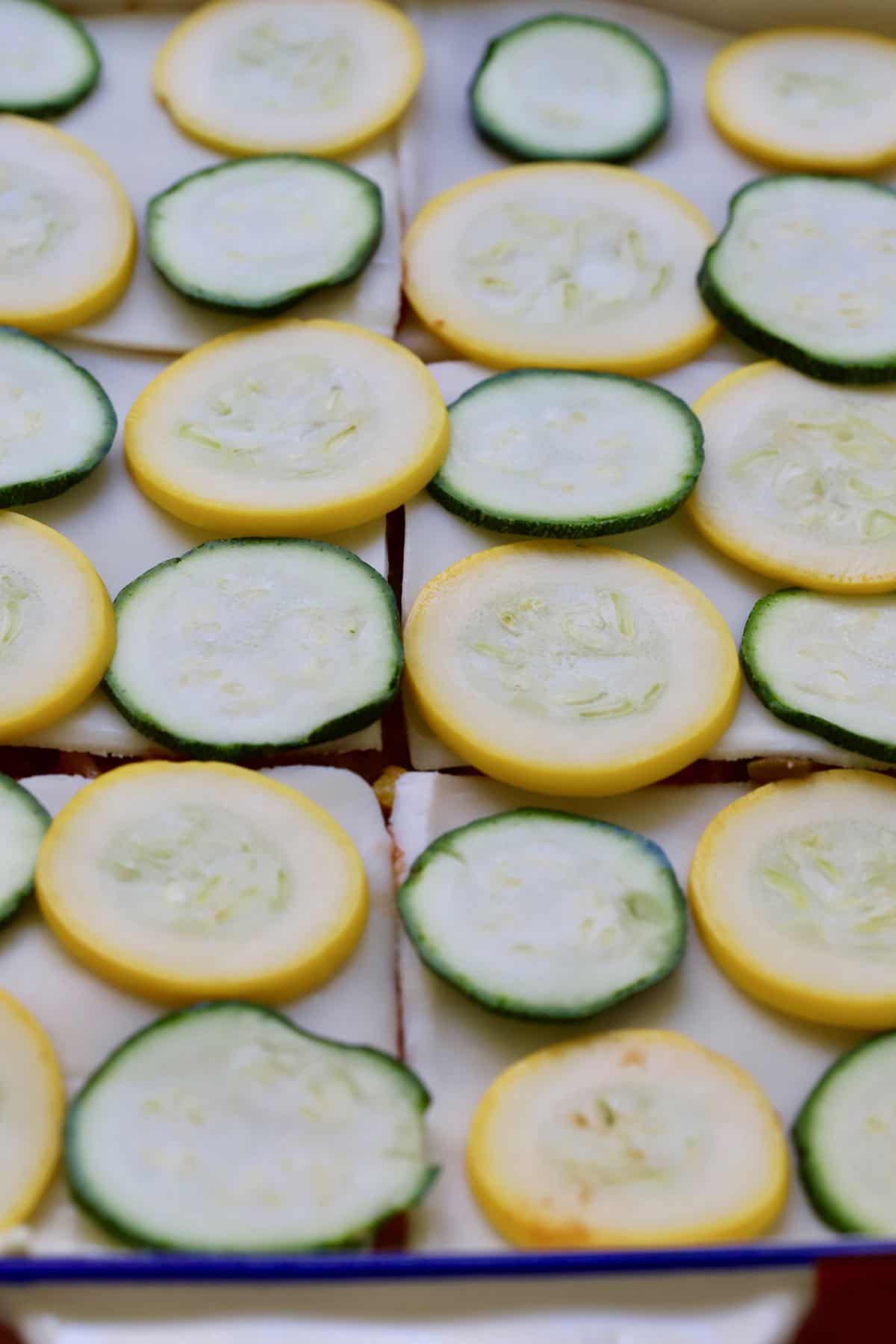 Sliced yellow and zucchini squash on top of mozzarella slices in a baking dish. 