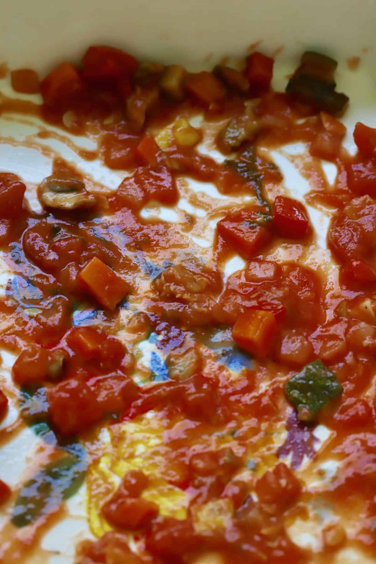 Tomato sauce with vegetables in the bottom of a baking dish. 