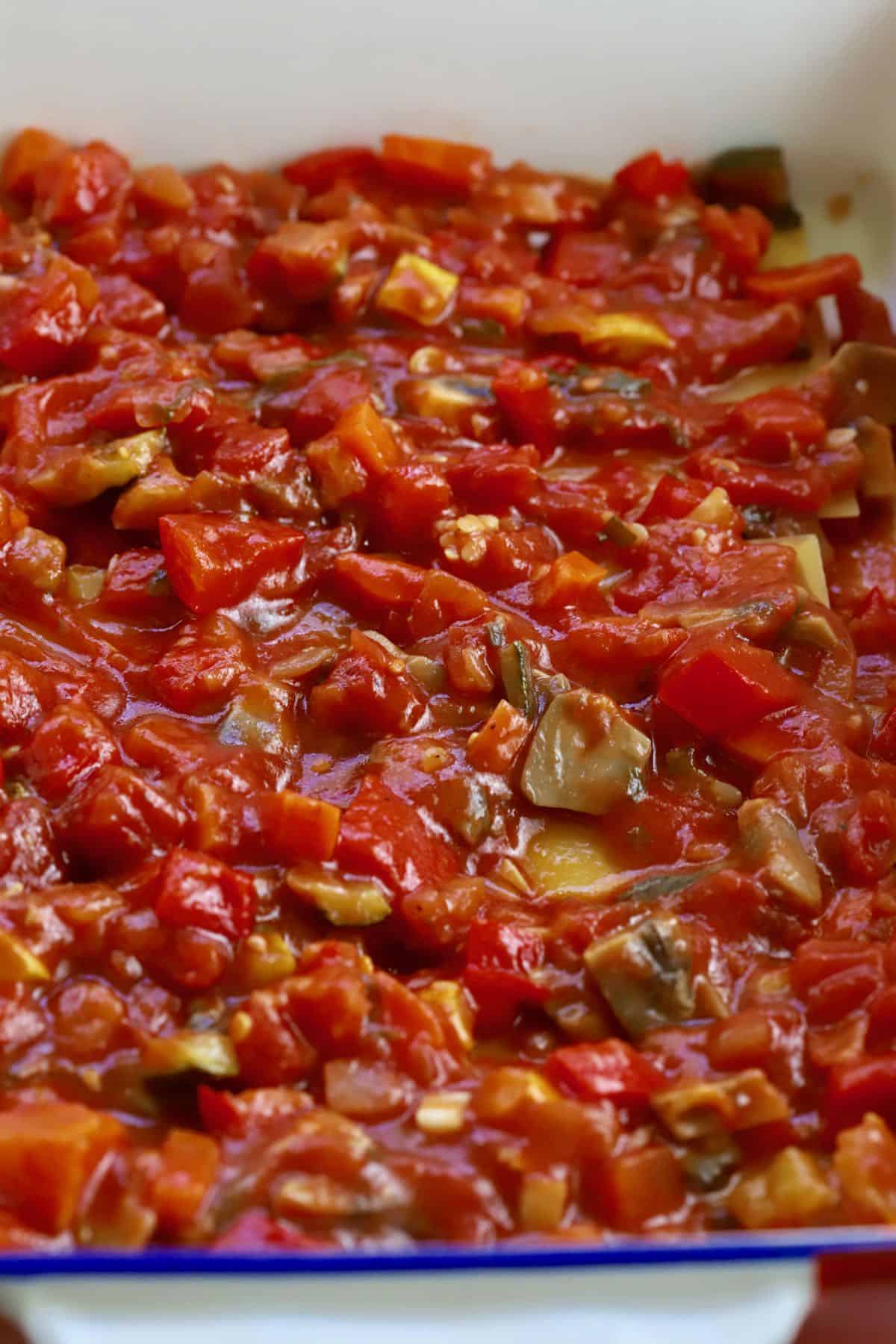 Tomato sauce with vegetables covering lasagna noodles in a baking dish. 