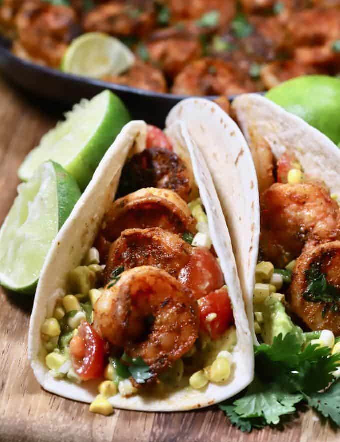 Shrimp tacos on a cutting board with lime halves. 