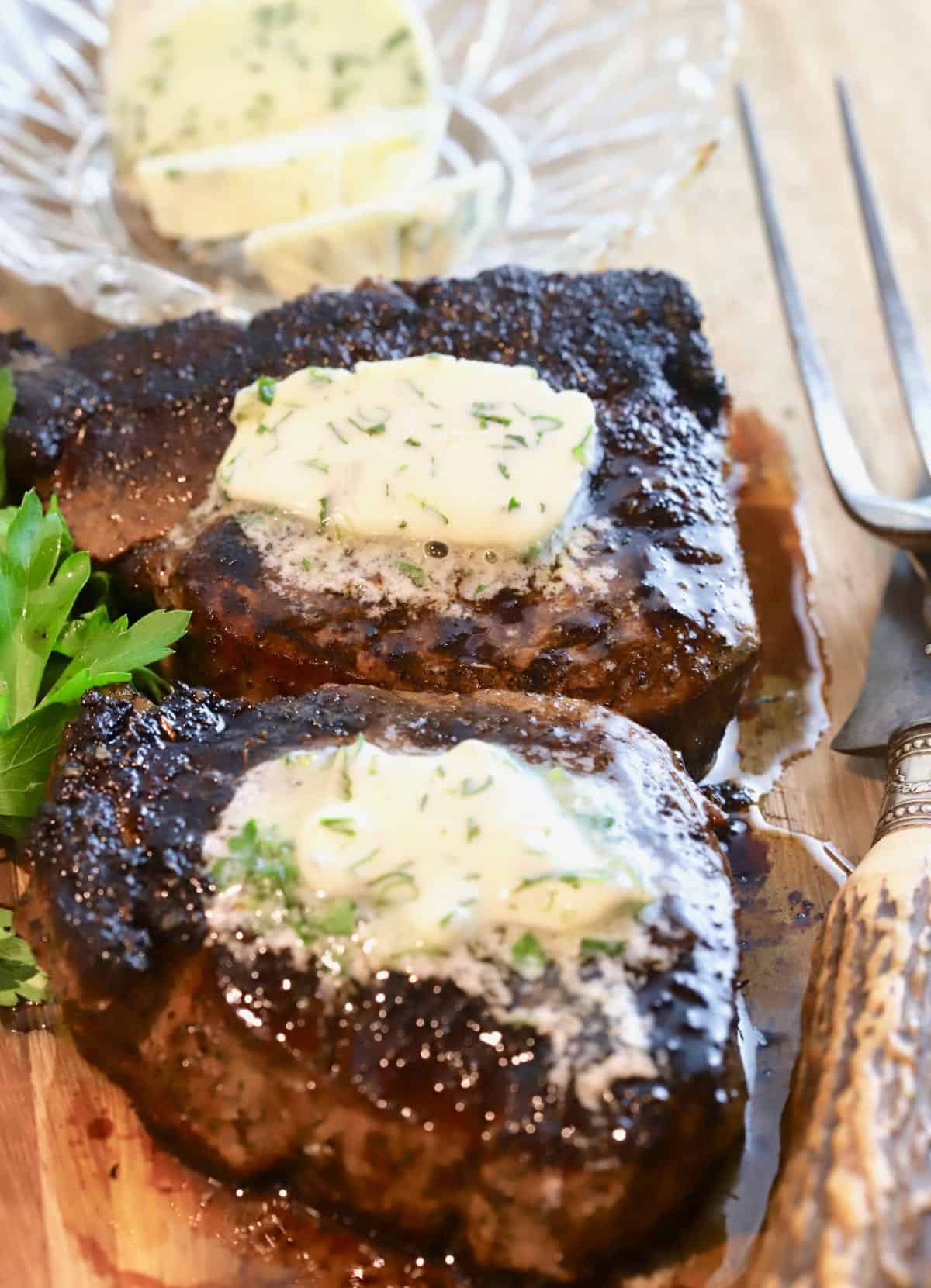 Two blackened steaks topped with garlic herb butter. 