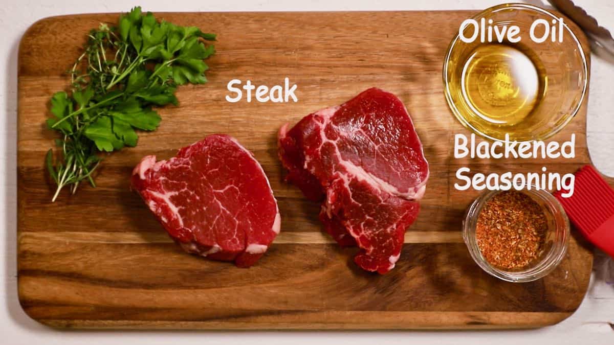 Two steaks on a wooden cutting board with parsley and olive oil. 