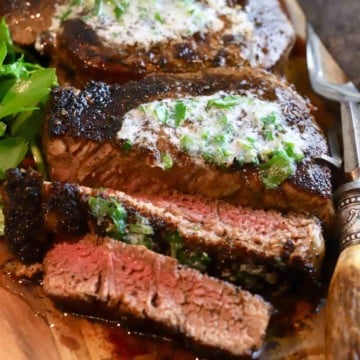 Two blackened steaks on a wooden cutting board.