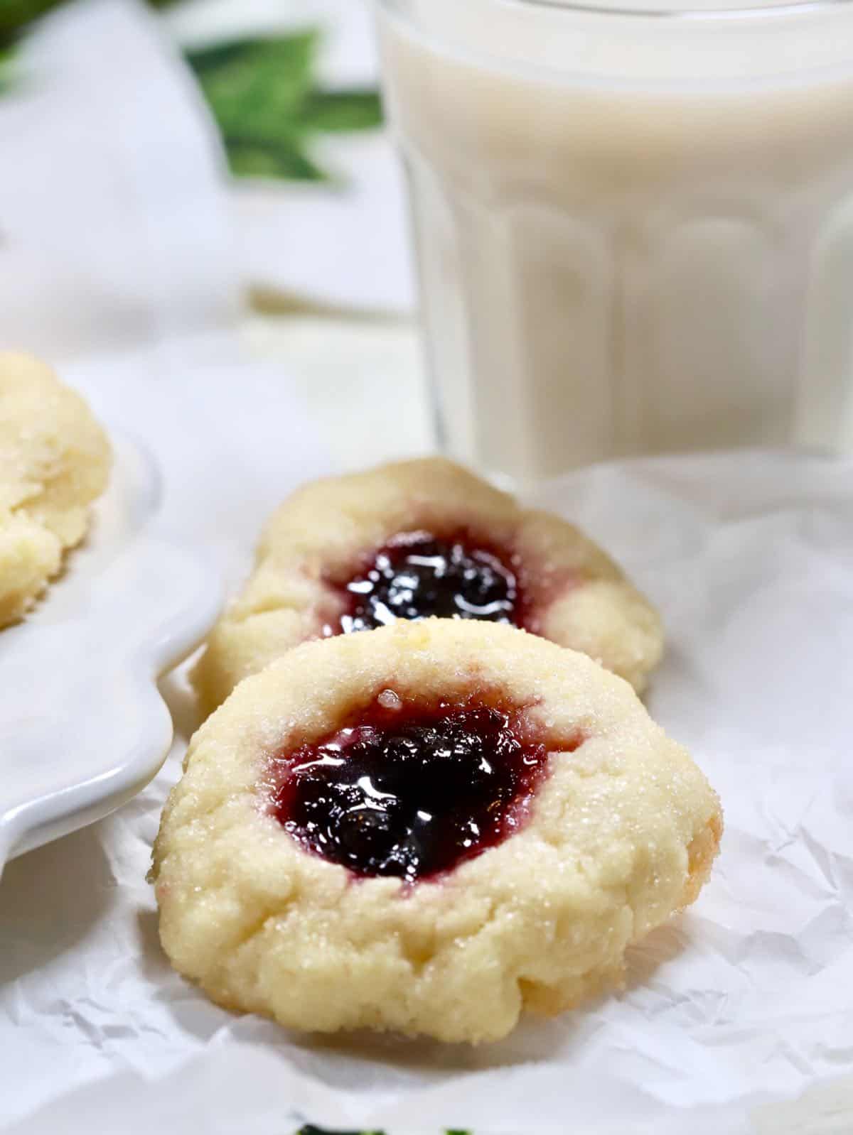 Two blueberry thumbprint cookies with a glass of milk. 