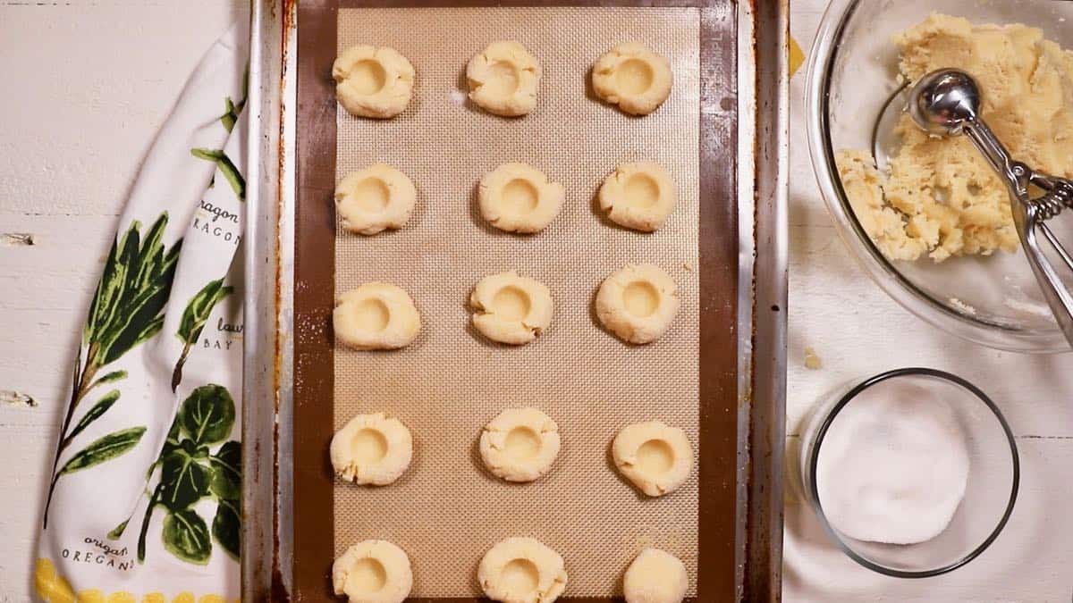 Shortbread dough on a cookie sheet with holes to hold jam. 