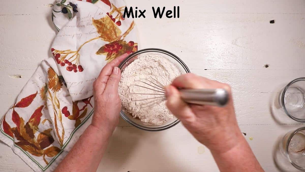 Mixing flour, baking soda and cinnamon in a bowl with a whisk.