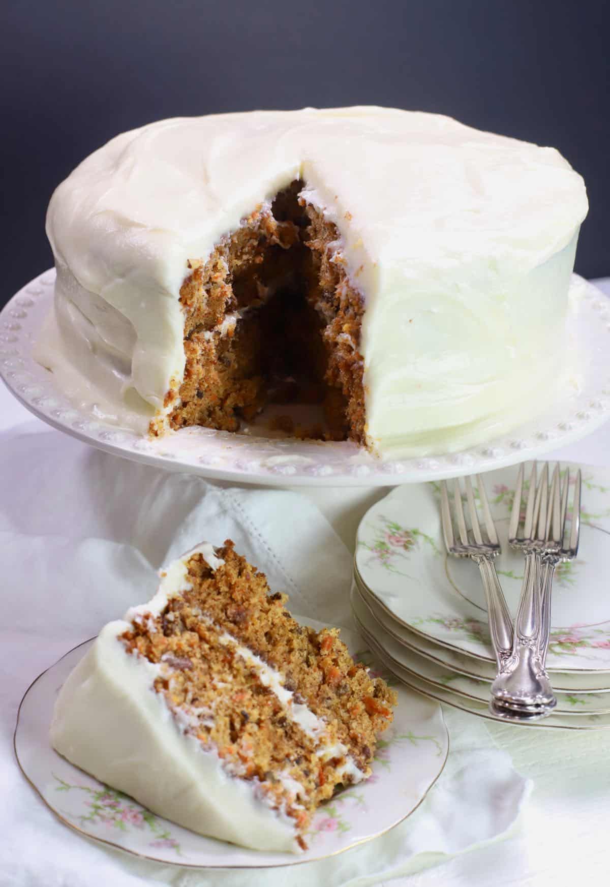 Carrot cake on a cake platter with a slice cut. 